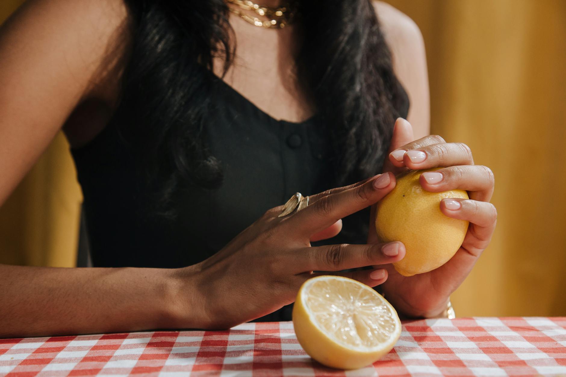 A woman holding a fresh lemon at a dining table, symbolizing natural, intentional approaches to intimacy and pleasure.