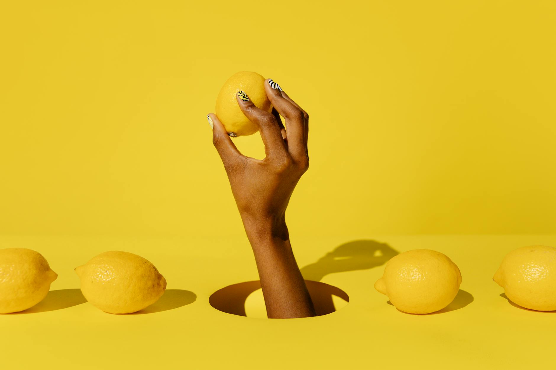 A hand holding a lemon against a vivid yellow background, representing fresh reconnection and embodied sensation