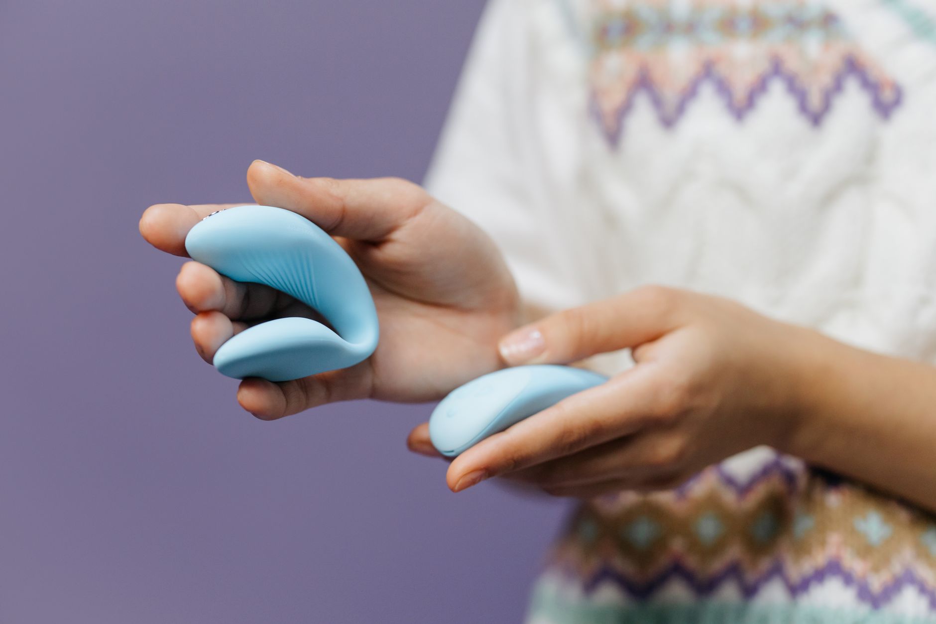 Close-up of hands holding a sleek blue vibrator against a purple background, representing intimate pleasure and novelty in long-term partnerships.