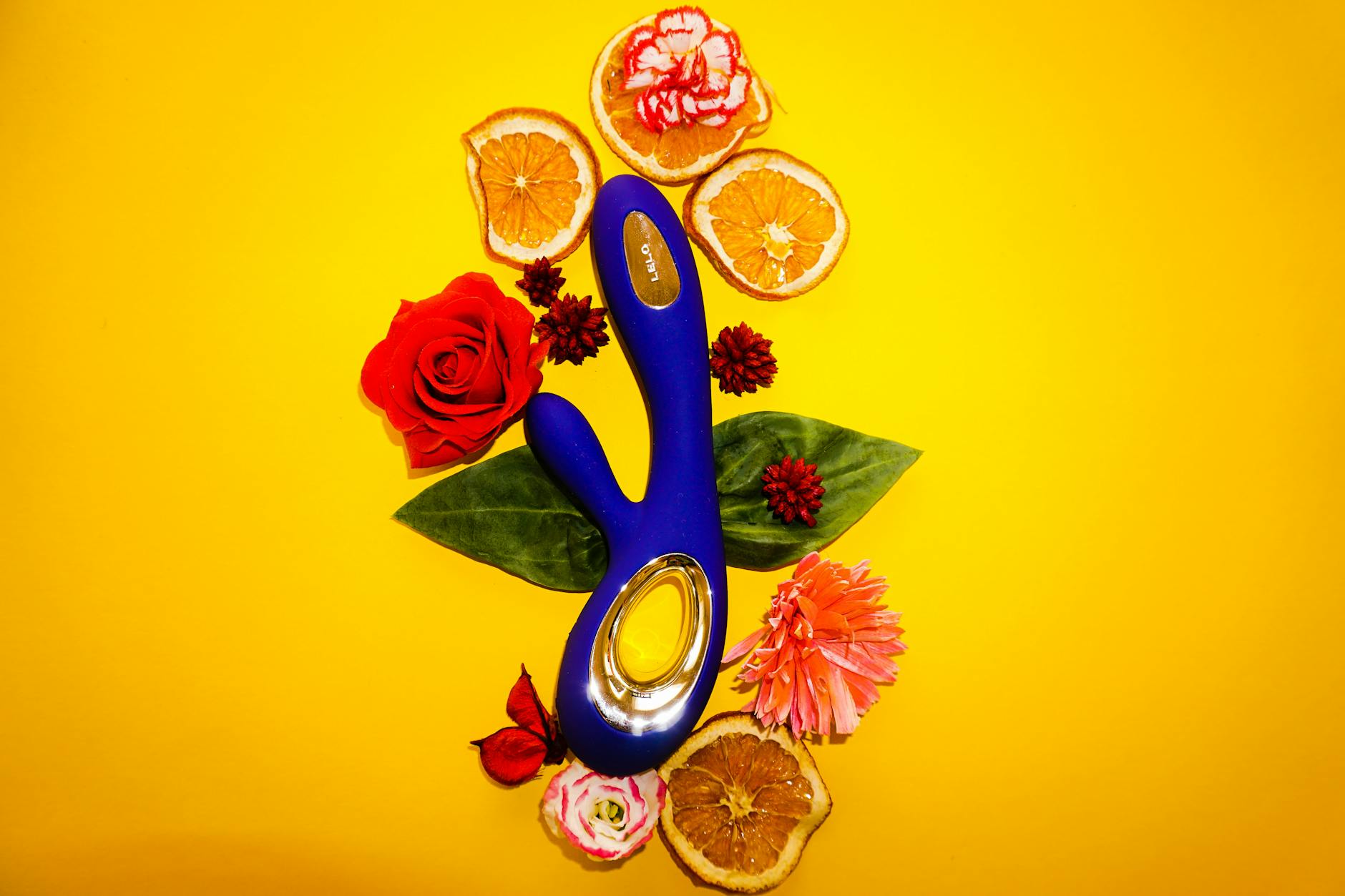 Vibrador de sucção de Limão contra fundo amarelo brilhante, rodeado por flores e fatias de laranja